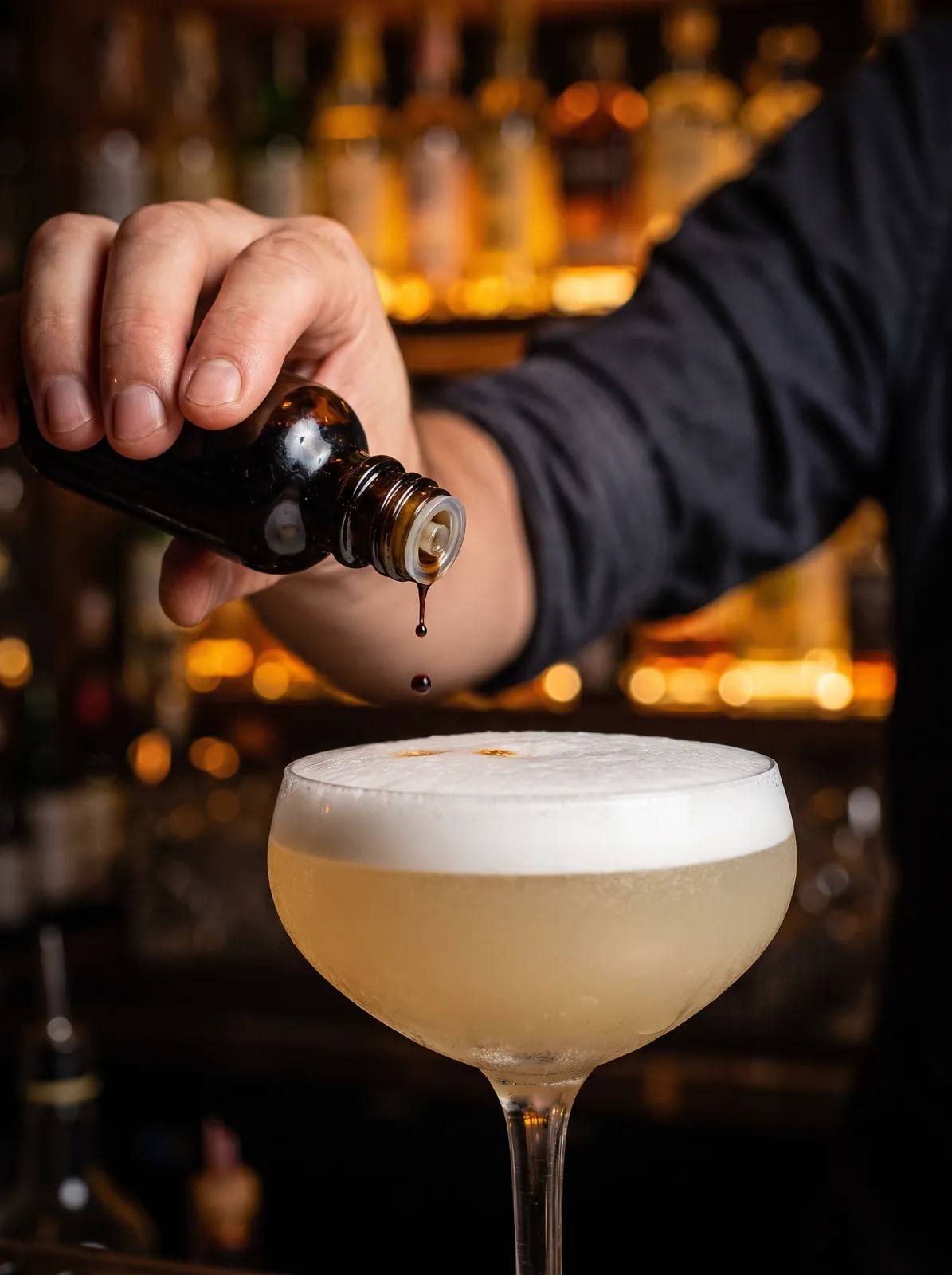 A bartender adds drops of bitters to the foam of a pisco sour