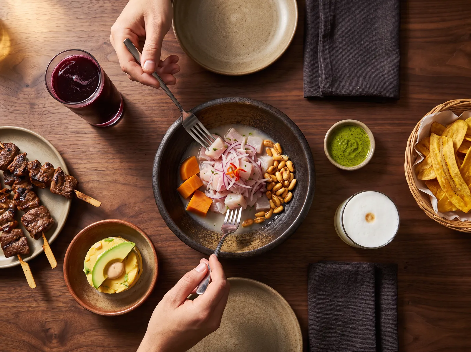 Overhead view of a ceviche bowl surrounded by shared plates, with two hands reaching in with forks